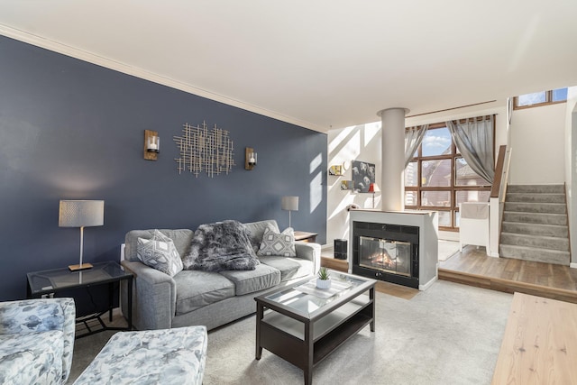 living room with crown molding, stairway, an accent wall, a glass covered fireplace, and baseboards