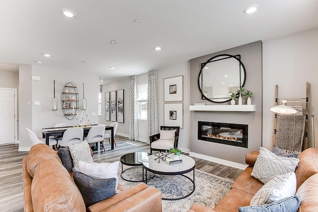 living room with baseboards, wood finished floors, a glass covered fireplace, and recessed lighting