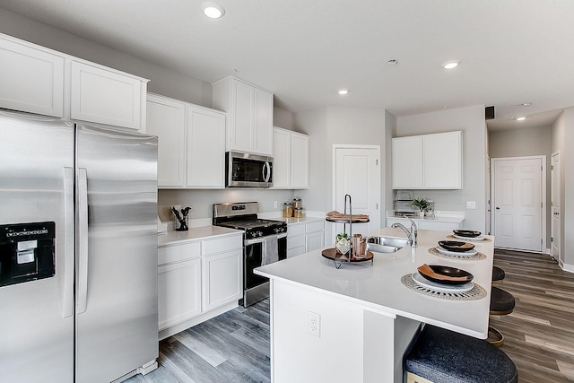 kitchen with appliances with stainless steel finishes, a kitchen bar, wood finished floors, and a kitchen island with sink