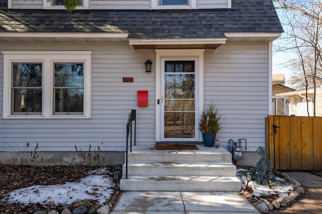 doorway to property featuring roof with shingles and fence