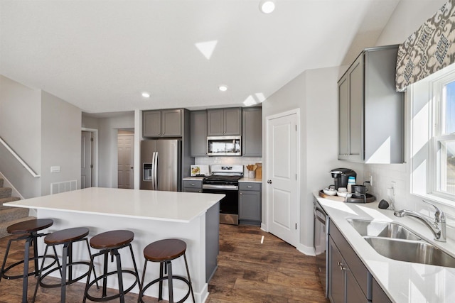 kitchen featuring a breakfast bar area, stainless steel appliances, a sink, light countertops, and gray cabinets