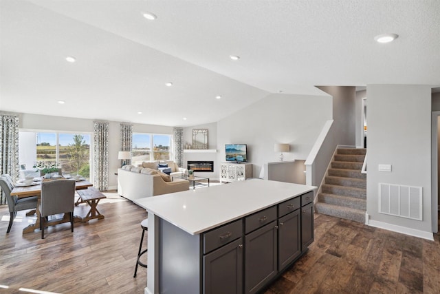 kitchen with a kitchen island, visible vents, open floor plan, light countertops, and a glass covered fireplace