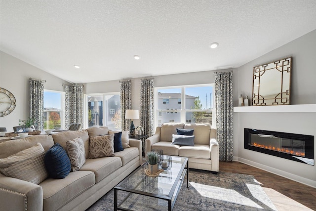 living room featuring vaulted ceiling, dark wood-type flooring, a glass covered fireplace, and a wealth of natural light