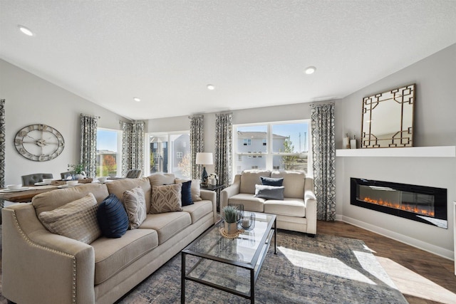 living room featuring dark wood finished floors, a glass covered fireplace, vaulted ceiling, a textured ceiling, and baseboards