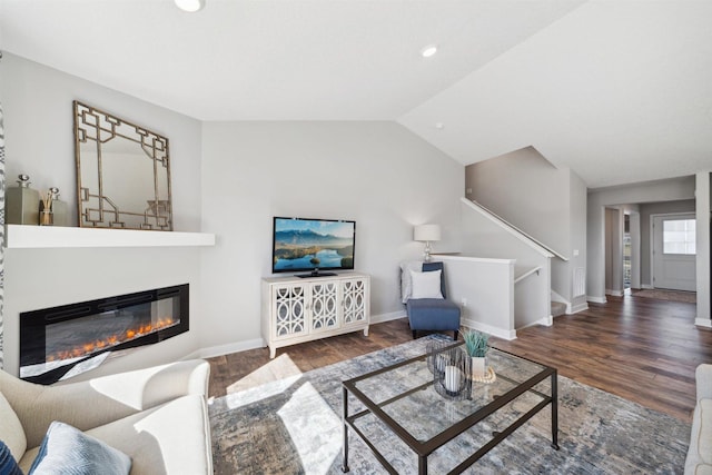 living room featuring vaulted ceiling, stairs, a glass covered fireplace, and dark wood finished floors