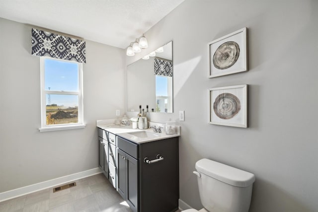 bathroom featuring toilet, a sink, visible vents, baseboards, and double vanity