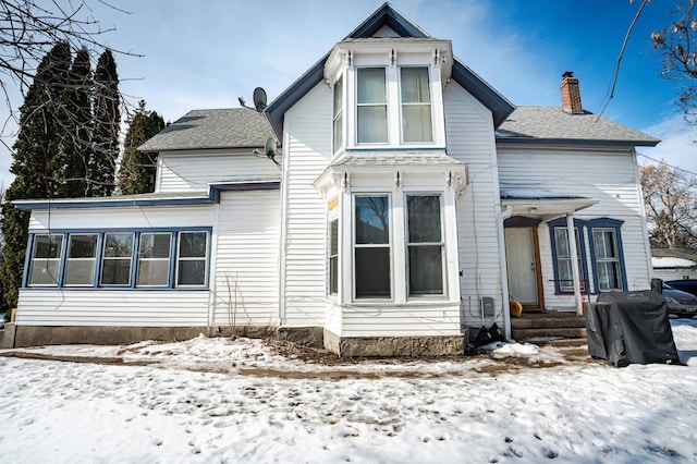 snow covered rear of property with roof with shingles and a chimney