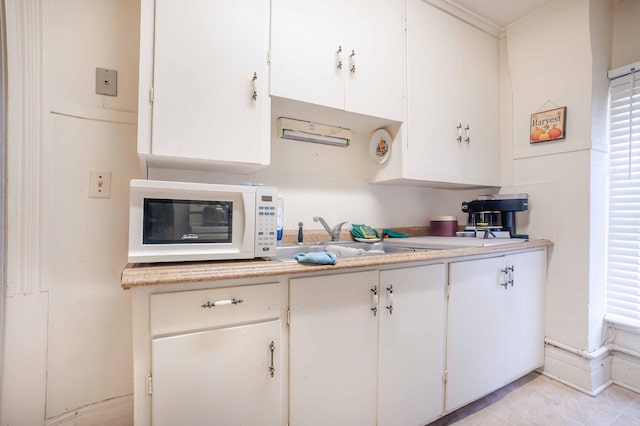 kitchen with white cabinets, white microwave, light countertops, and a sink