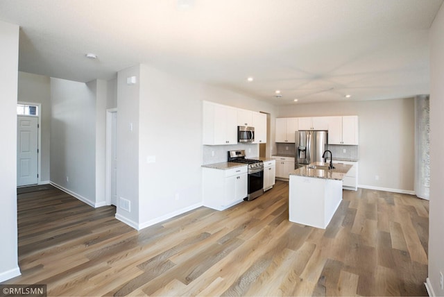 kitchen with appliances with stainless steel finishes, light stone countertops, a kitchen island with sink, white cabinetry, and a sink