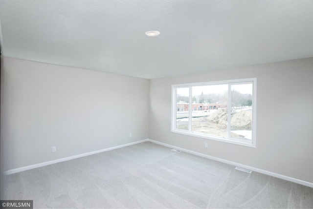 spare room with light colored carpet, visible vents, and baseboards