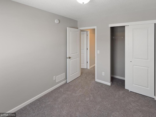 unfurnished bedroom with a textured ceiling, carpet flooring, visible vents, baseboards, and a closet