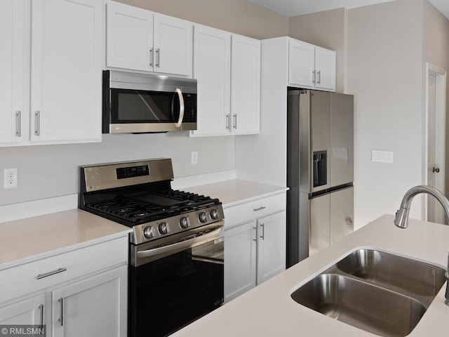 kitchen with stainless steel appliances, light countertops, a sink, and white cabinetry