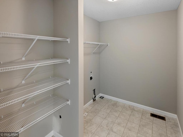 laundry room with visible vents, electric dryer hookup, tile patterned flooring, laundry area, and baseboards