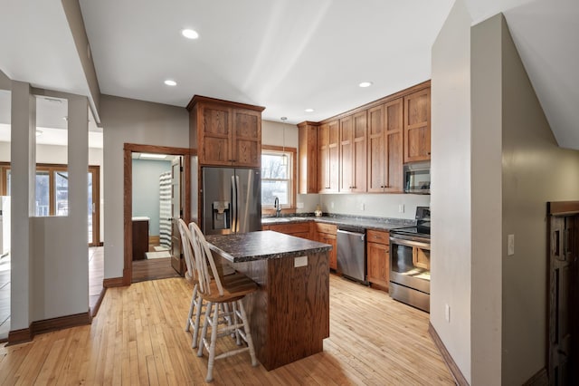 kitchen featuring a kitchen bar, a sink, dark countertops, stainless steel appliances, and light wood finished floors