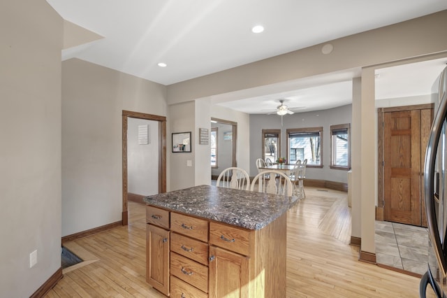 kitchen with dark stone countertops, a center island, recessed lighting, light wood finished floors, and baseboards