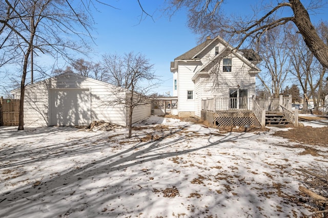 snow covered rear of property with an outbuilding, fence, a wooden deck, a chimney, and a garage