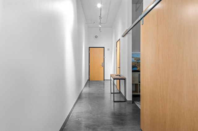 hall featuring rail lighting, a high ceiling, attic access, concrete floors, and baseboards