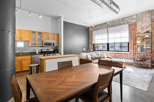 dining area featuring radiator, a towering ceiling, track lighting, brick wall, and concrete floors