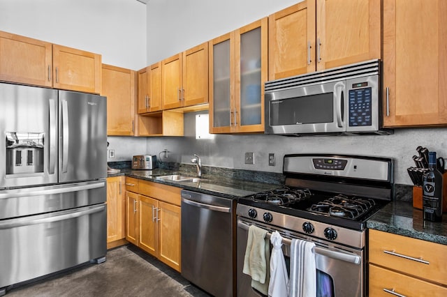 kitchen featuring glass insert cabinets, stainless steel appliances, a sink, and dark stone counters