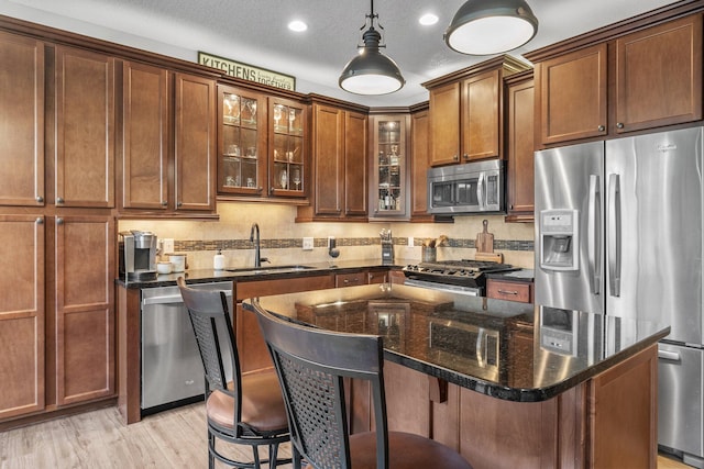 kitchen featuring stainless steel appliances, light wood-style floors, glass insert cabinets, a sink, and a kitchen breakfast bar