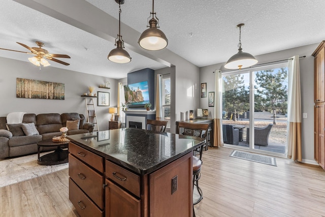 kitchen with light wood-style flooring, a kitchen breakfast bar, open floor plan, decorative light fixtures, and a fireplace