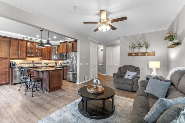 living area featuring baseboards, ceiling fan, a textured ceiling, and light wood finished floors