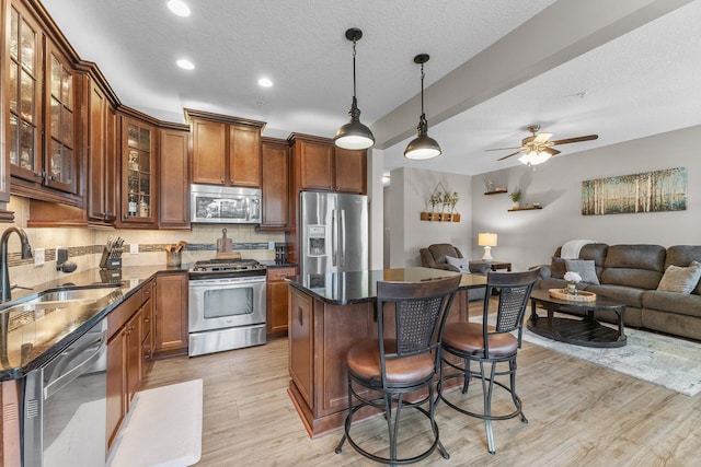 kitchen with appliances with stainless steel finishes, a breakfast bar, open floor plan, light wood-type flooring, and a sink