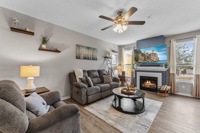 living area with a textured ceiling, a glass covered fireplace, wood finished floors, and a wealth of natural light