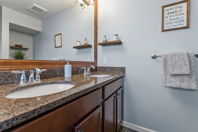 bathroom featuring double vanity, a textured ceiling, visible vents, and a sink