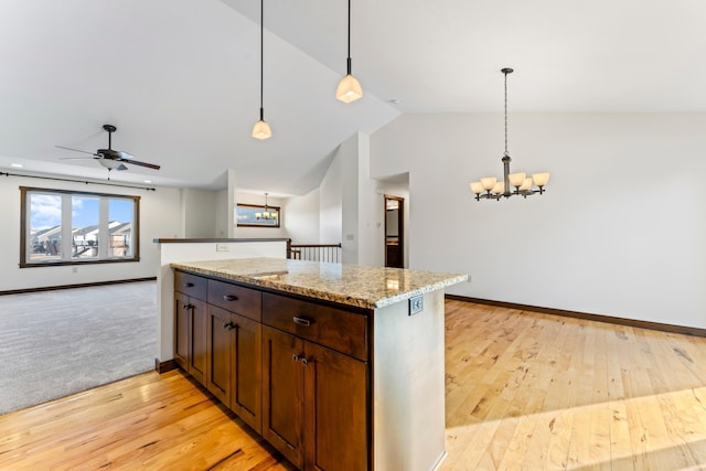 kitchen featuring lofted ceiling, light stone counters, open floor plan, decorative light fixtures, and light wood-style floors