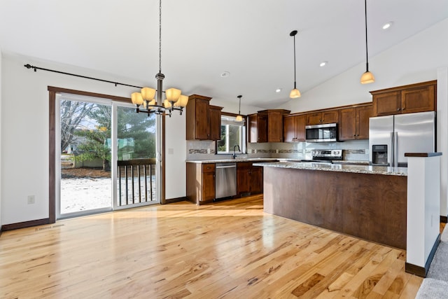 kitchen featuring tasteful backsplash, light wood-style flooring, a kitchen island, hanging light fixtures, and stainless steel appliances