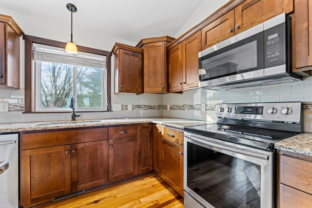 kitchen with light stone counters, stainless steel appliances, visible vents, hanging light fixtures, and a sink