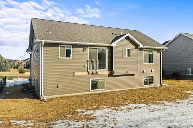 snow covered house with central air condition unit and a shingled roof