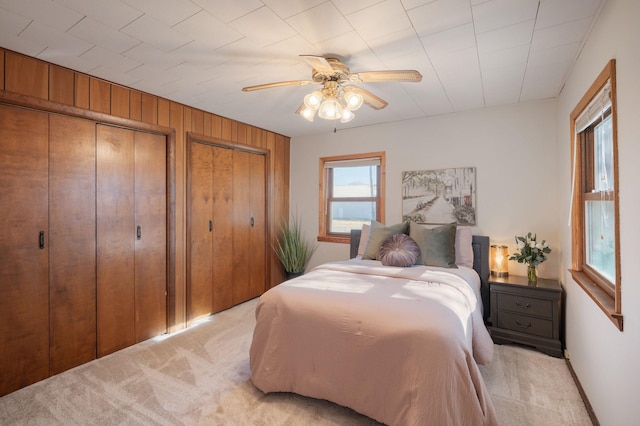 bedroom featuring a ceiling fan, light carpet, wooden walls, and two closets