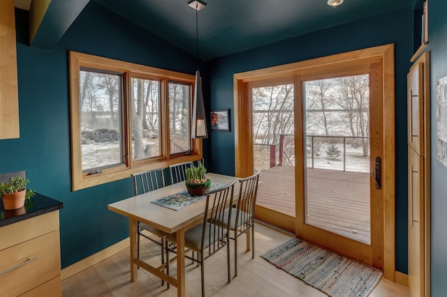 dining space with vaulted ceiling, light wood-style flooring, and baseboards