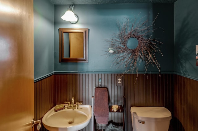 half bathroom with a wainscoted wall, a sink, wood walls, and toilet