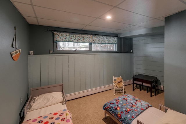 living area featuring carpet floors, wood walls, a baseboard radiator, and a drop ceiling