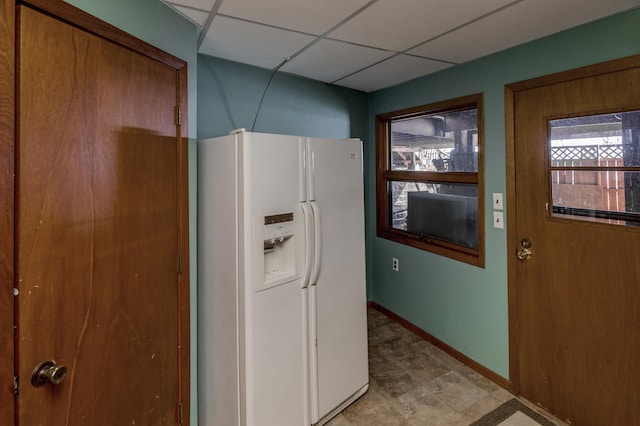 kitchen featuring white fridge with ice dispenser, baseboards, and a drop ceiling