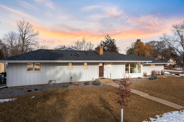 ranch-style home featuring central air condition unit, board and batten siding, a chimney, and a yard