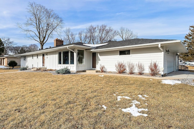 ranch-style home featuring an attached garage, a chimney, a front yard, and board and batten siding