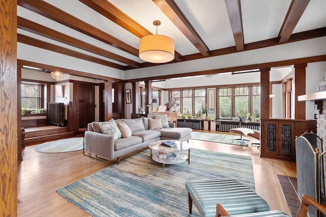 living area with a fireplace with flush hearth, wood finished floors, beam ceiling, and a healthy amount of sunlight