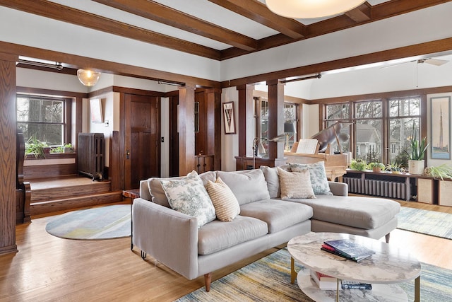 living room with beam ceiling, radiator heating unit, decorative columns, and light wood-style floors