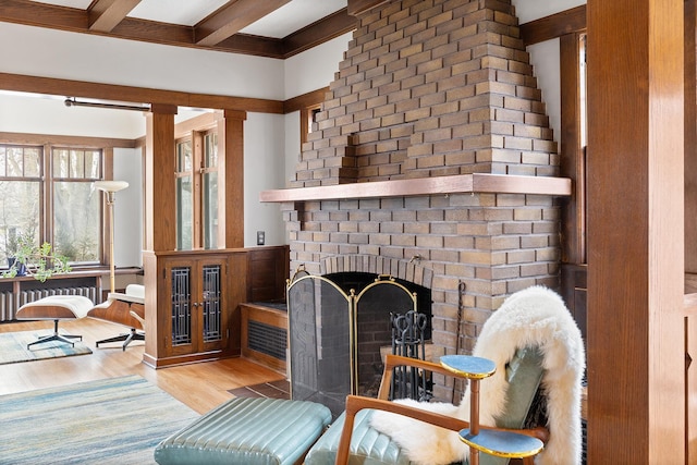 living area featuring beam ceiling, a brick fireplace, radiator heating unit, and wood finished floors