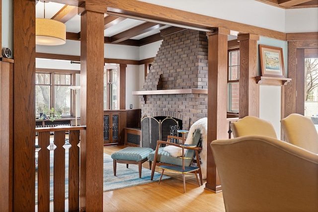 living area with a brick fireplace, beam ceiling, decorative columns, and wood finished floors