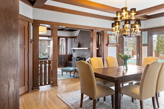 dining space featuring a fireplace, light wood-style floors, a chandelier, beamed ceiling, and ornate columns