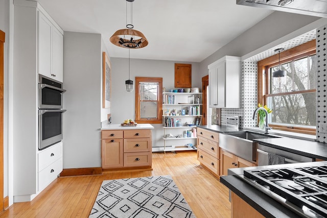 kitchen with dishwashing machine, hanging light fixtures, light wood-type flooring, double oven, and a sink