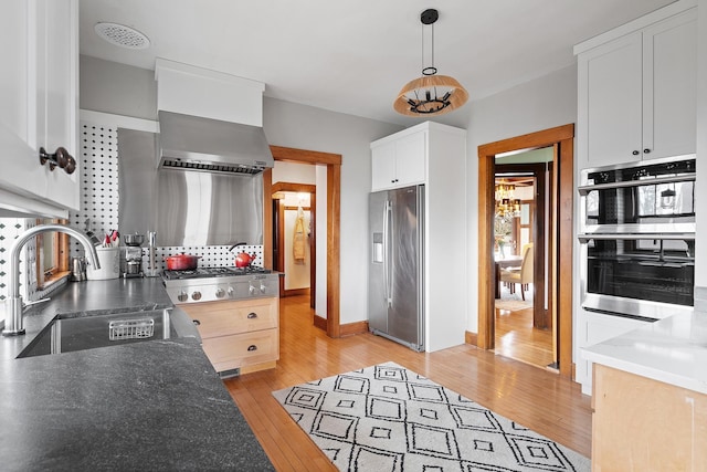 kitchen featuring white cabinets, wall chimney exhaust hood, appliances with stainless steel finishes, light wood-style floors, and a sink