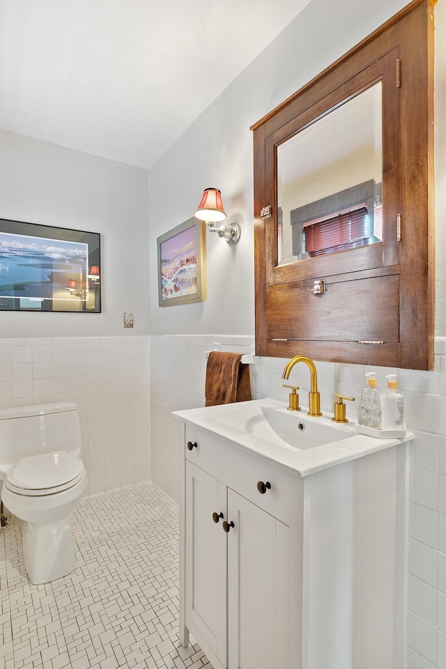 half bath with tile walls, toilet, wainscoting, vanity, and tile patterned flooring