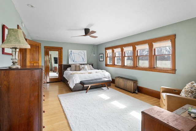 bedroom featuring multiple windows, radiator heating unit, light wood-type flooring, and baseboards