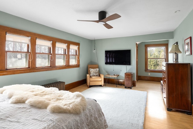 bedroom featuring a ceiling fan, radiator heating unit, light wood-style flooring, and baseboards